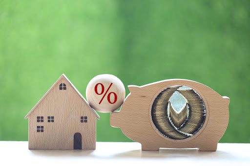 Mortgage rates and Real estate concept, Stack of coins money in piggy bank wood and Model house with percentage symbol icon on natural green background