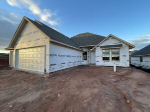 A single-story house under construction with visible insulation labeled BEACON. The building site shows bare earth and a clear sky in the background.