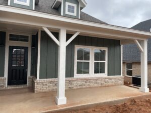 A newly constructed house with a green and brick exterior, white trim, and a concrete porch.