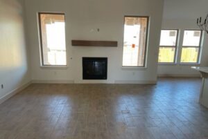 Empty living room with a tiled floor, fireplace, and two windows. Walls are painted light gray.