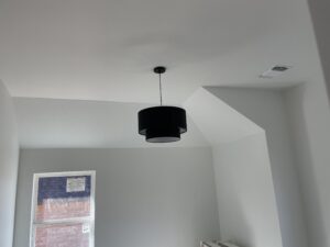 Minimalist room with white walls and ceiling, featuring a black pendant light. A window on the left shows a partial view of a brick building.