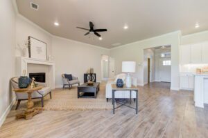 A spacious living room with a ceiling fan, light wood flooring, a fireplace, and modern furniture. Walls are painted in a soft neutral color.