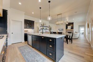 Modern kitchen with a black island, white countertops, pendant lights, and hardwood flooring. Dining area and living room visible in the background.