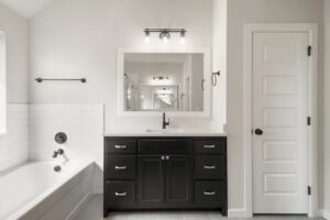 Modern bathroom featuring a black vanity cabinet, white bathtub, and multiple mirrors on a tiled wall, with a closed white door.