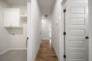 A clean, modern hallway with white doors, grey walls, and wooden floors, featuring built-in white cabinetry on the left.