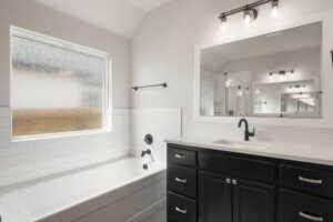 Modern bathroom interior featuring a black vanity, white bathtub, frosted window, and a view into a tiled shower area.
