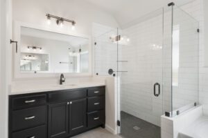 Modern bathroom with white walls, black vanity, large mirror, and glass shower enclosure.