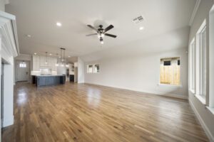 Spacious, empty living room with hardwood floors, leading to an open kitchen with a central island, and ample natural light from windows.