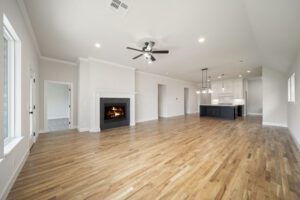 Spacious modern living room with a fireplace, hardwood floors, white walls, and an adjoining kitchen with a black island.