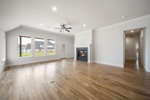 Spacious, modern living room with hardwood floors, white walls, a fireplace, ceiling fan, and large windows.
