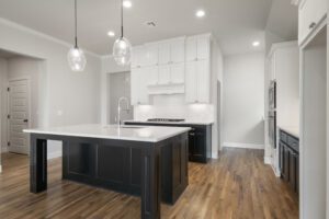 Modern kitchen interior featuring white cabinets, a black island, stainless steel appliances, hardwood floors, and pendant lights.