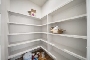 An empty walk-in closet with white shelves, a few boxes, and paint cans on the floor.