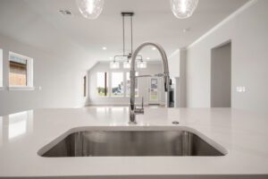 Modern kitchen interior with a stainless steel sink and chrome faucet, white countertops, and elegant pendant lights.