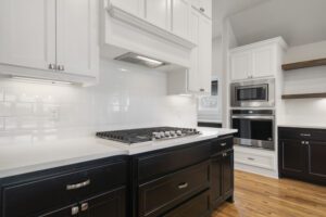 A modern kitchen with white upper cabinets, dark lower cabinets, stainless steel appliances, a gas stove, and hardwood floors.
