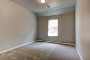 Empty room with taupe walls, a single window, and beige carpeted floor.