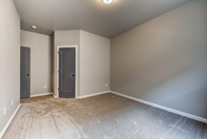 An empty room with gray walls, carpeted floor, and two closed dark doors.