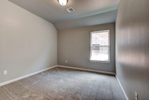 Empty modern room with gray walls, one window, and beige carpet flooring.