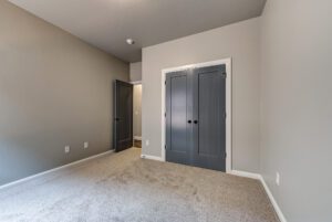 Interior of a room with taupe walls, gray carpet, and two closed gray doors, one leading into another room.