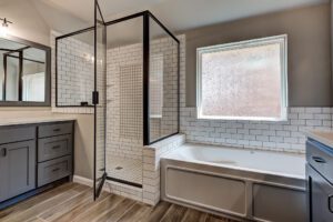 Modern bathroom with a glass-enclosed shower, white subway tiles, and a gray vanity cabinet, under natural light from a frosted window.