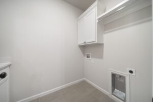 Empty laundry room with white cabinets, gray tiled floor, and a small pet door at the bottom of the wall.