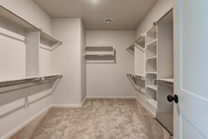 Empty walk-in closet with beige carpet, white walls, and built-in shelving units.