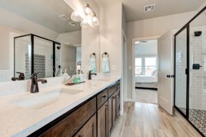 Modern bathroom interior featuring dual sinks, large mirrors, and a view into a bedroom through an open door. bright, clean design with decorative tiles and wooden cabinets.