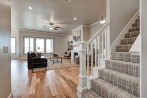 A bright living room with hardwood floors, a staircase with carpeted steps, modern furniture, and neutral decor.