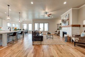 Spacious living room with hardwood floors, modern furniture, a white brick fireplace, kitchen bar stools, and pendant lighting.