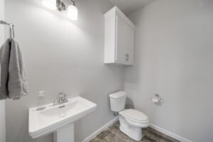 A small, modern bathroom with a white pedestal sink, toilet, wall-mounted cabinet, and towel hanging on the left.