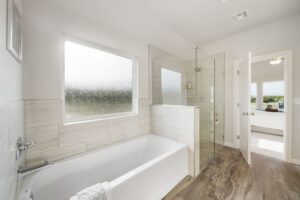 Modern bathroom with a bathtub, glass shower, and textured window bringing in natural light.