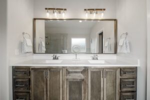 Modern bathroom featuring a large mirror, dual sinks, rustic wooden cabinets, and decorative lighting.