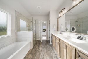 Modern bathroom with dual sinks, large mirrors, a bathtub, and a separate shower area, featuring wooden cabinetry and tiled walls.