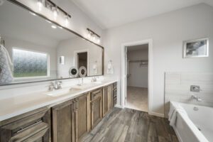 A modern bathroom with dual sinks, wooden cabinets, a large mirror, and an adjoining walk-in closet.