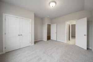 Empty residential room with gray carpet, white walls, and multiple closed white doors, including closet and entryways.