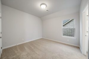 Empty room with beige carpet, white walls, and a single window with a view of a brick wall outside.