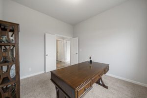Empty modern room with a wooden desk, bookshelf, carpet flooring, and white walls featuring double doors.