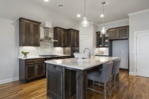 Modern kitchen with dark wood cabinets, white marble backsplash, stainless steel appliances, an island with bar stools, and pendant lighting.