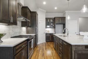 Modern kitchen interior with dark wooden cabinets, white countertops, stainless steel appliances, and hardwood floors.
