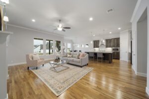 Spacious, modern living room with hardwood floors, gray walls, ceiling fan, and contemporary furniture, leading to an open kitchen with a bar.