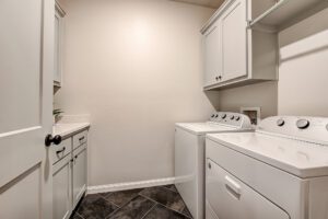 A neat laundry room with white appliances, cabinets, and a tiled floor, under warm lighting.