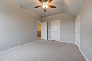 Empty room with gray carpet, white walls, ceiling fan, and three closed doors.