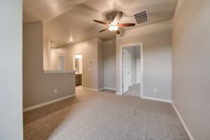 Empty room with beige carpet, white walls, ceiling fan, and an open door leading to another room.