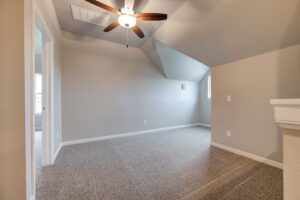 Empty room with slanted ceiling, a ceiling fan, gray walls, and carpeted flooring.