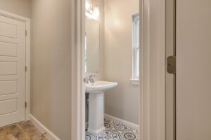A small bathroom with a pedestal sink, decorative floor tiles, and a wall-mounted light fixture above a mirror.