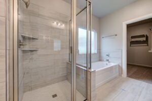 Modern bathroom with a glass shower stall next to a white bathtub, featuring gray tiled walls and flooring.