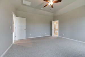 Empty room with beige carpet, gray walls, ceiling fan, and two white doors, one partially open leading to another room.