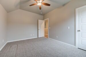 Empty residential room with gray walls and carpet, featuring a ceiling fan and open white doors.