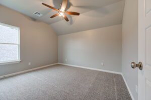 Empty room with beige walls and carpet, one window, and a ceiling fan.
