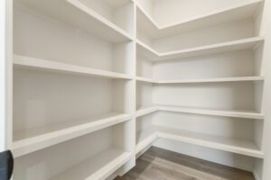 Empty white built-in corner shelves in a room with wooden flooring.