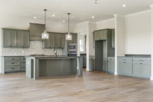 Modern kitchen with gray cabinetry, stainless steel appliances, a central island, and hardwood flooring under pendant lighting.